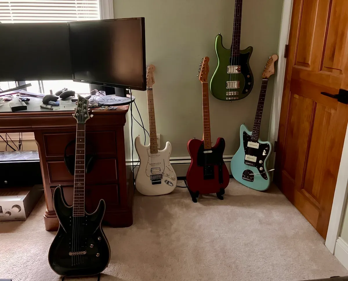 Five electric guitars and a bass on stands and hung on the wall of Andrew's room.