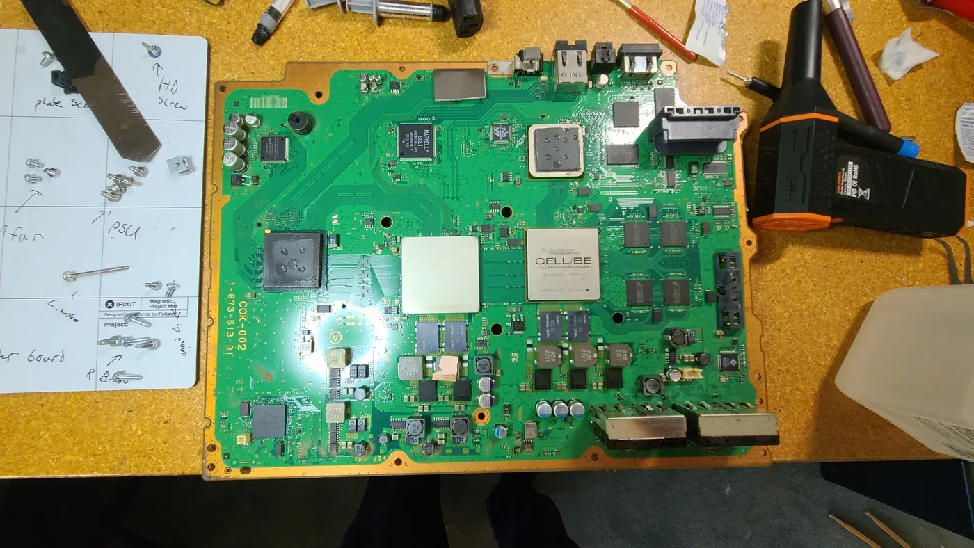 A PlayStation 3 motherboard on an iFixit project mat, with fresh thermal paste on the Cell and RSX chips.